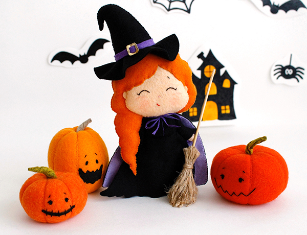 Felt hand sewn PDF tutorial with patterns by FeltCraftsFairyland - witch doll in pointed hat with broomstick in the hand and 3 orange spooky Halloween pumpkins are standing in front of the watercolor painted Halloween ornaments - bat and witch house, front view